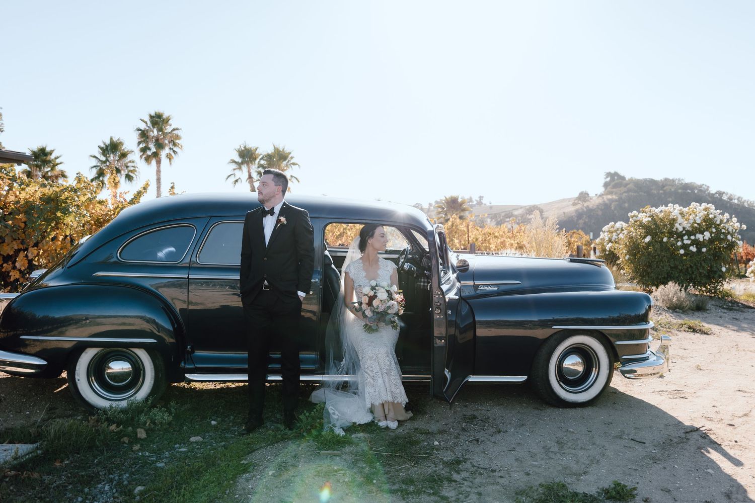 A bride with flowing veil and groom walk across a rolling green golf course.