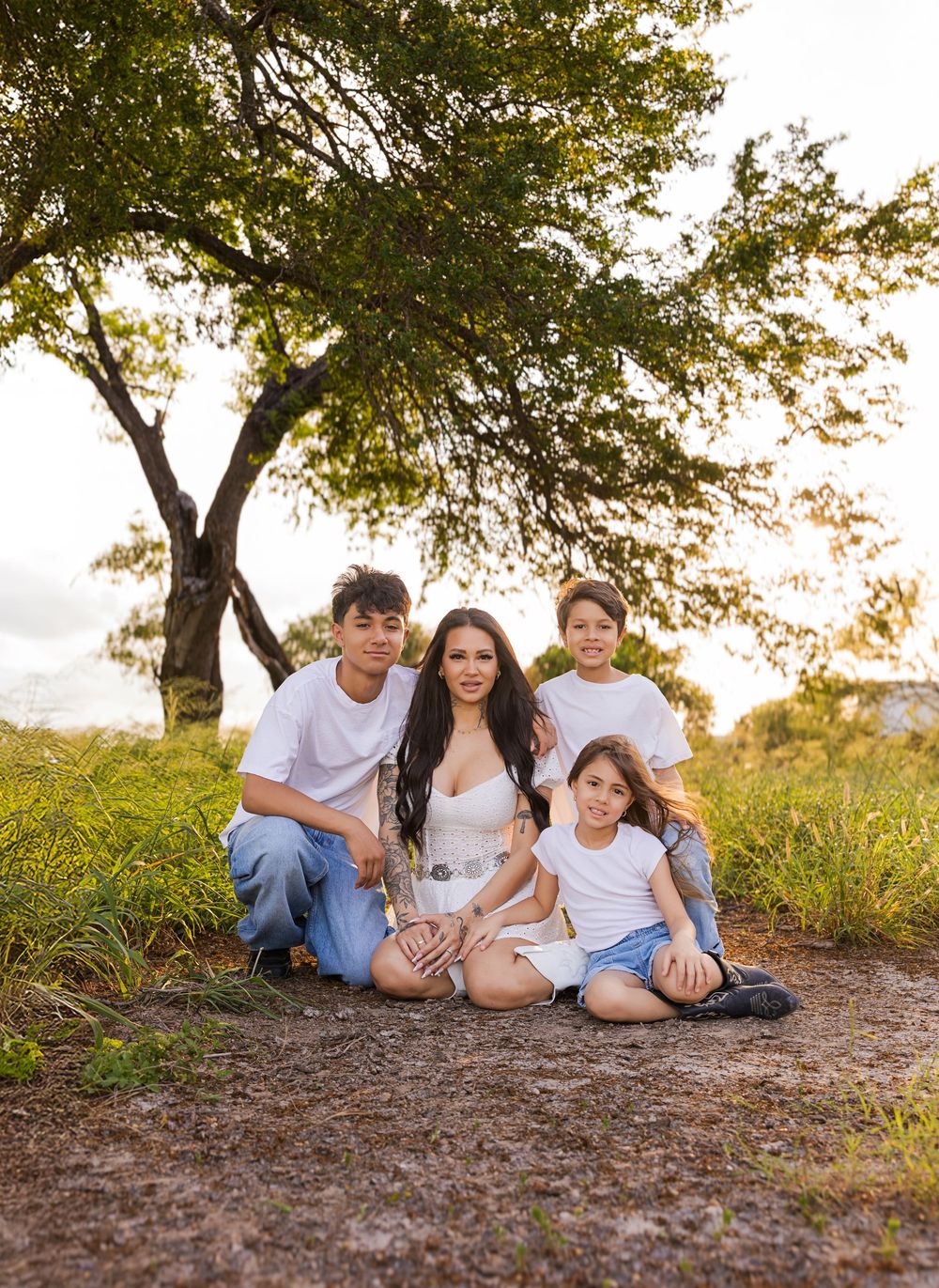 A family sits together on a dirt path surrounded by lush greenery during golden hour at sunset.