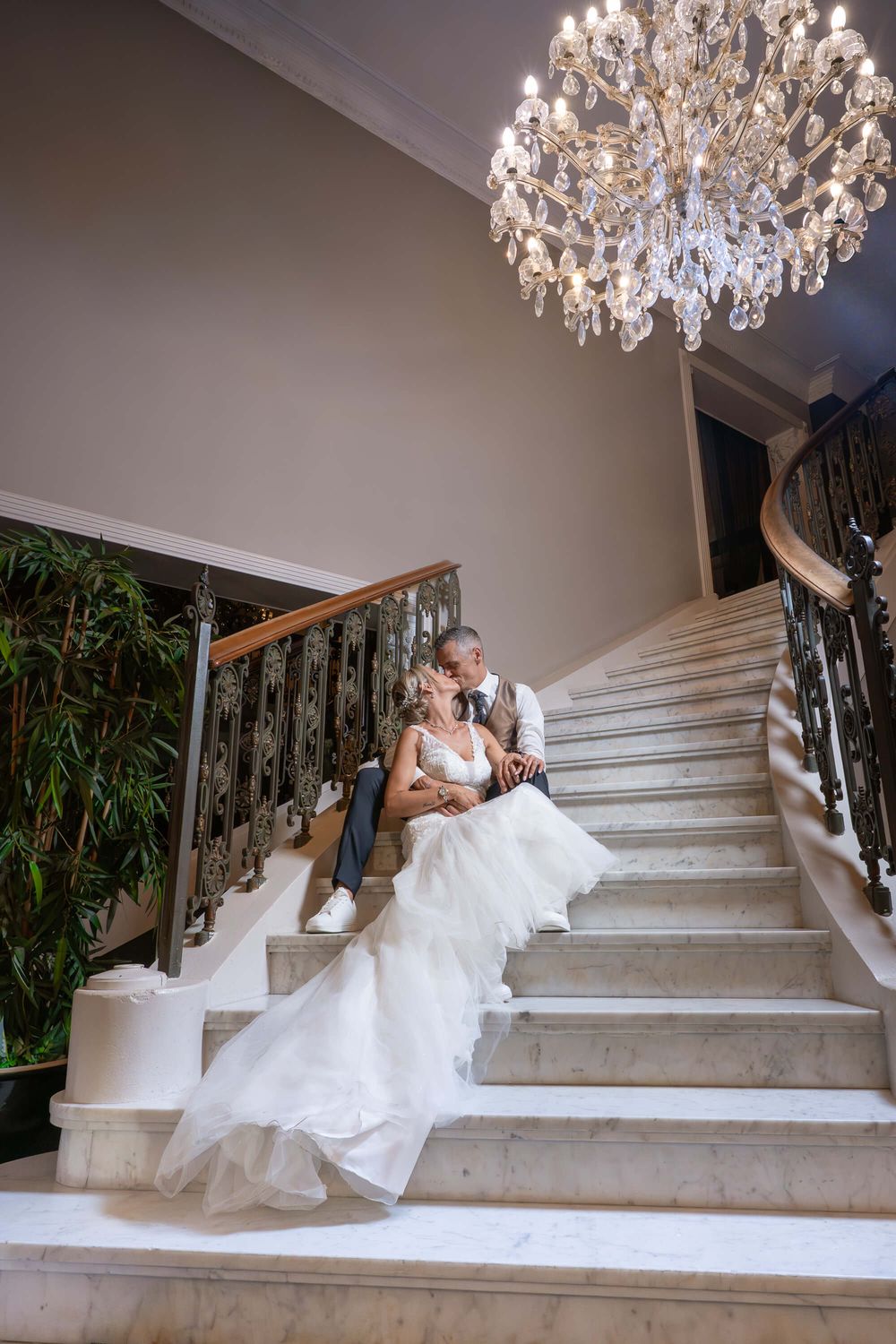 Mariés dans l’escalier du Petit Versailles à Charleroi, un instant d’amour et d’élégance capturé avec finesse pour célébrer leur journée uni