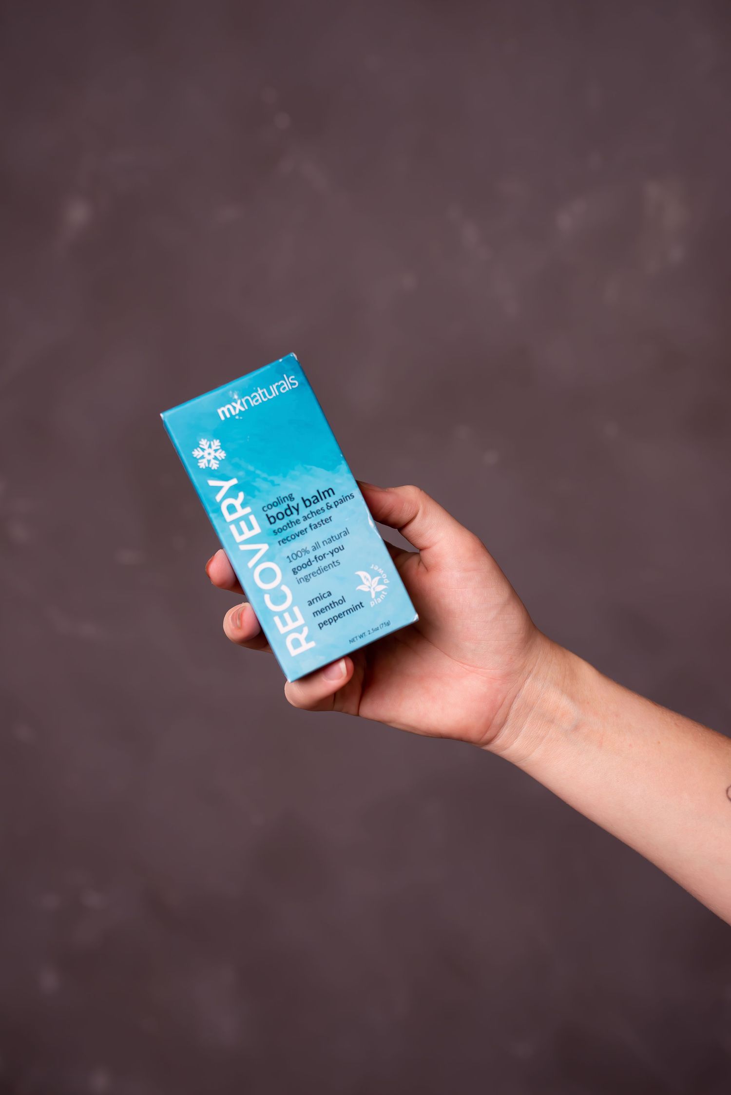 A hand holds a blue Recovery RX product box against a grey background.