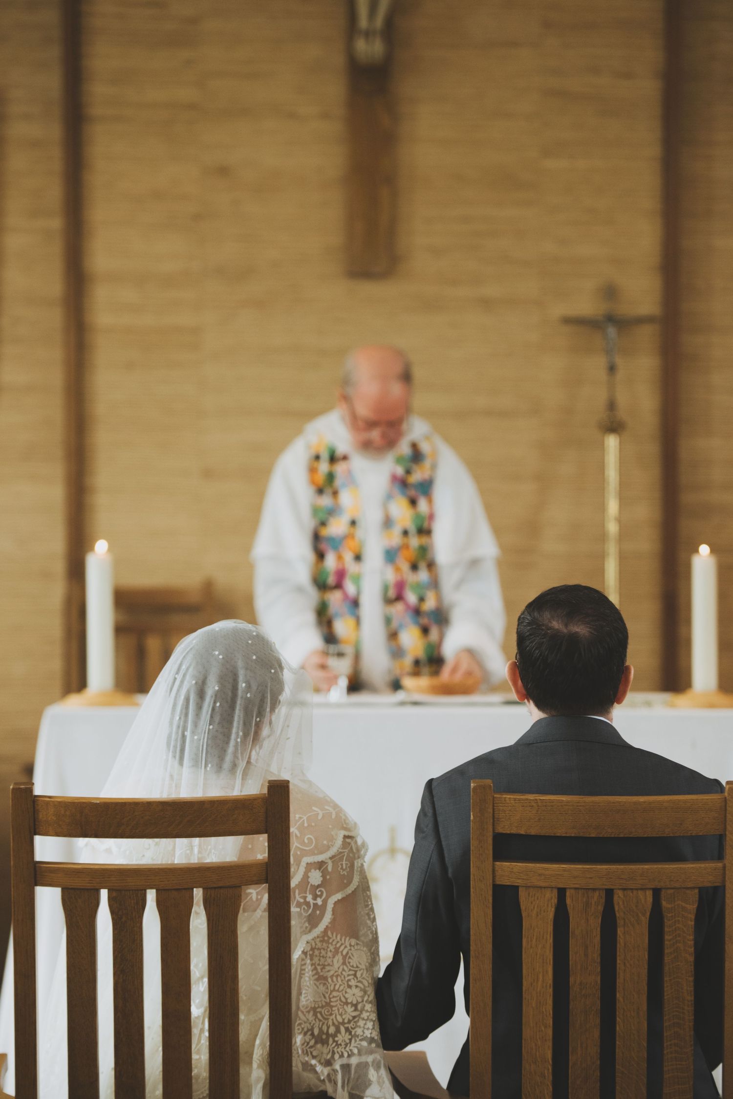 a bride and groom sit during their mass wedding ceremony and witness the priest prepare the Eucharist.