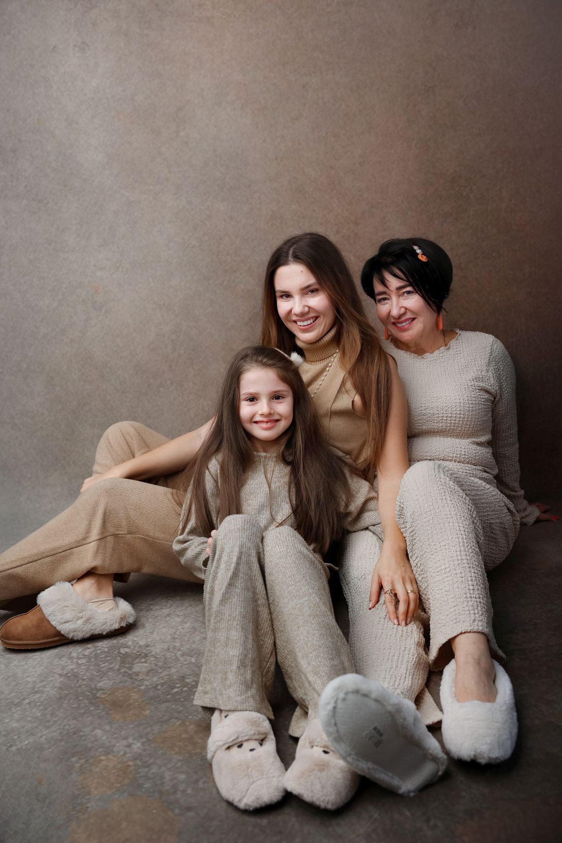 Three people in cozy neutral outfits sit together for a casual portrait.