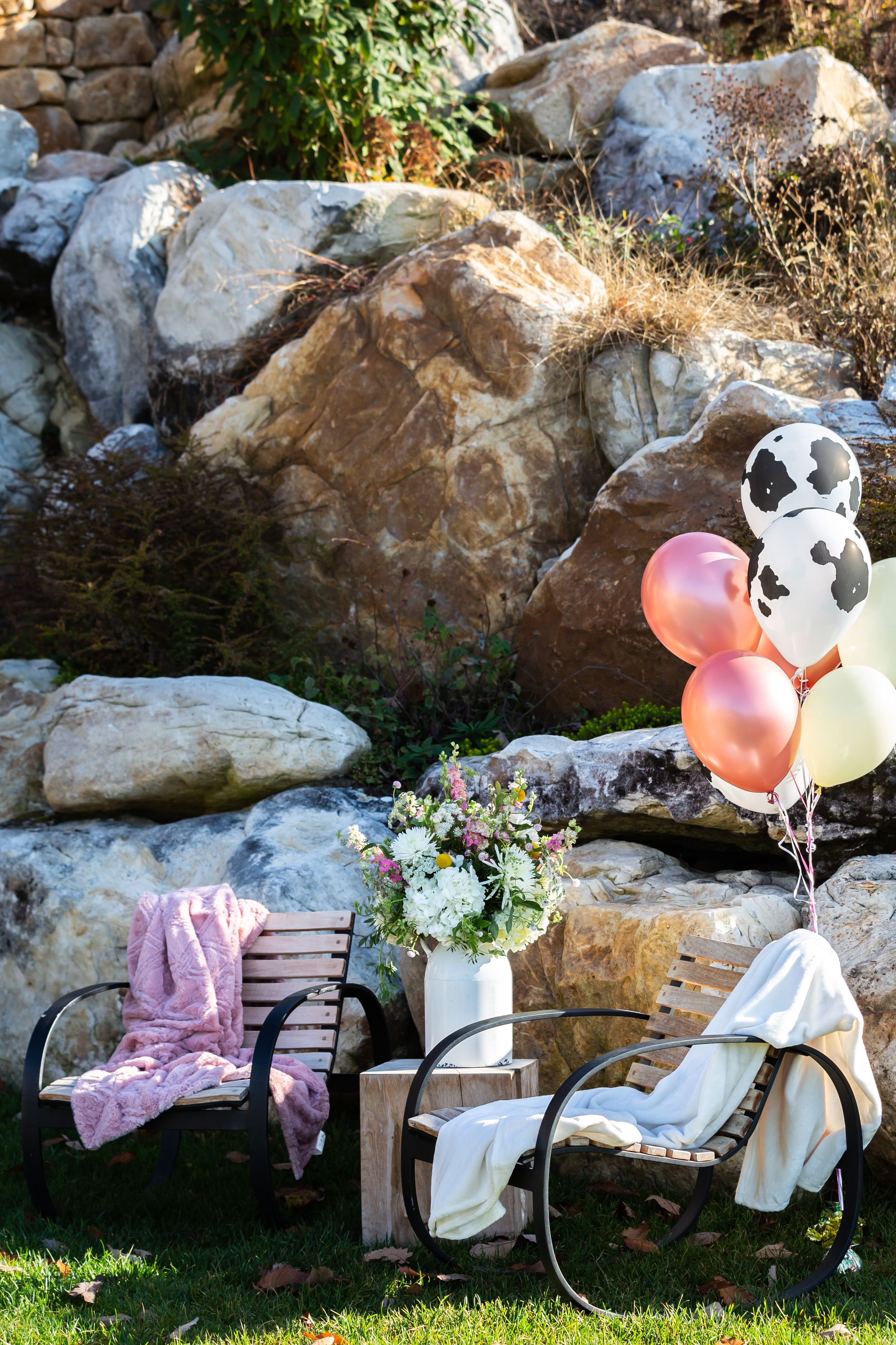 Outdoor seating area with balloons and floral arrangements against a rocky backdrop.