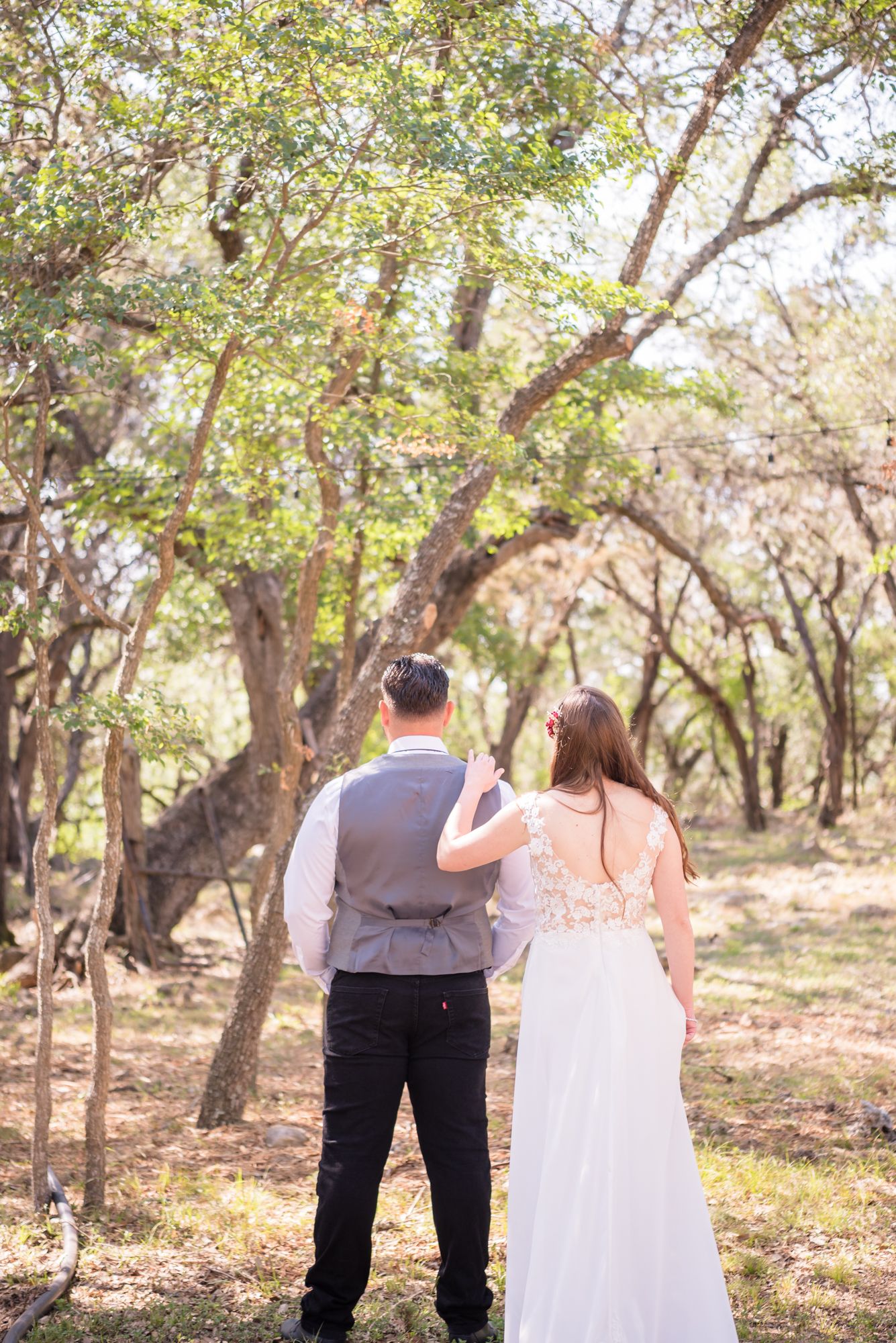 A couple stands together in a wooded setting wearing wedding attire on their special day.