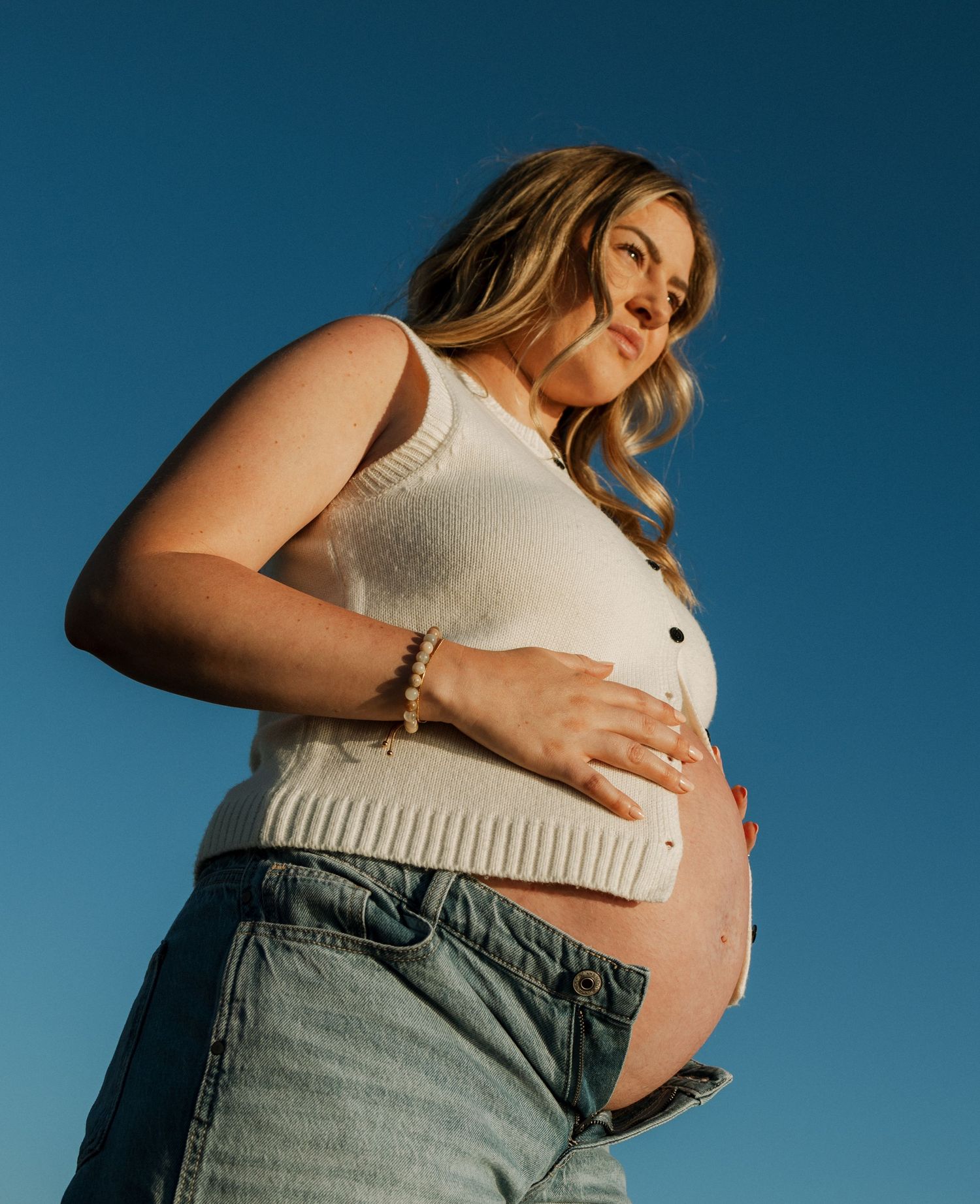 A series of maternity photos showing a pregnant woman in a white top and jeans against a blue background.