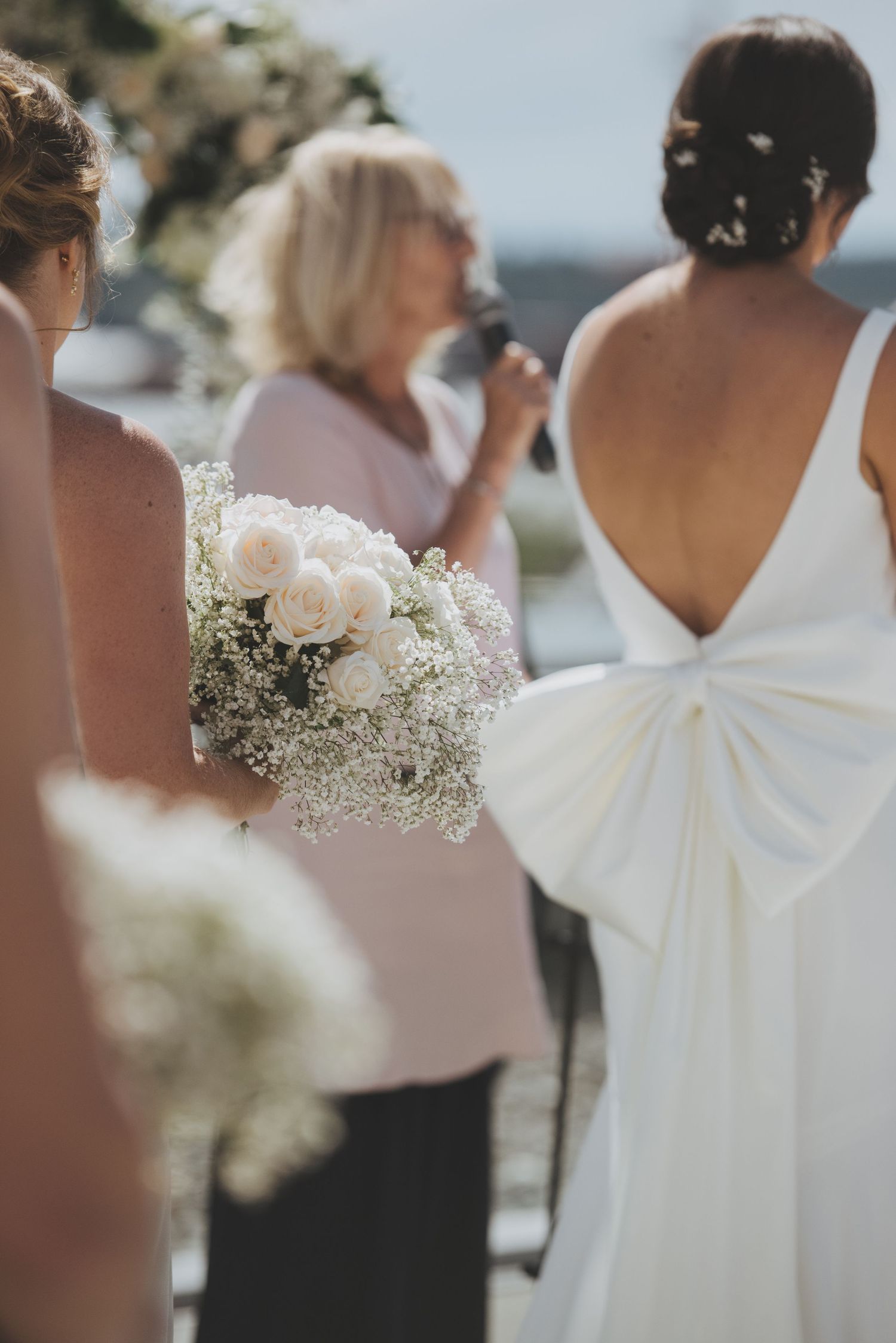 Detail shot of a bride in white dress with baby's breath and rose bouquet during outdoor ceremony.