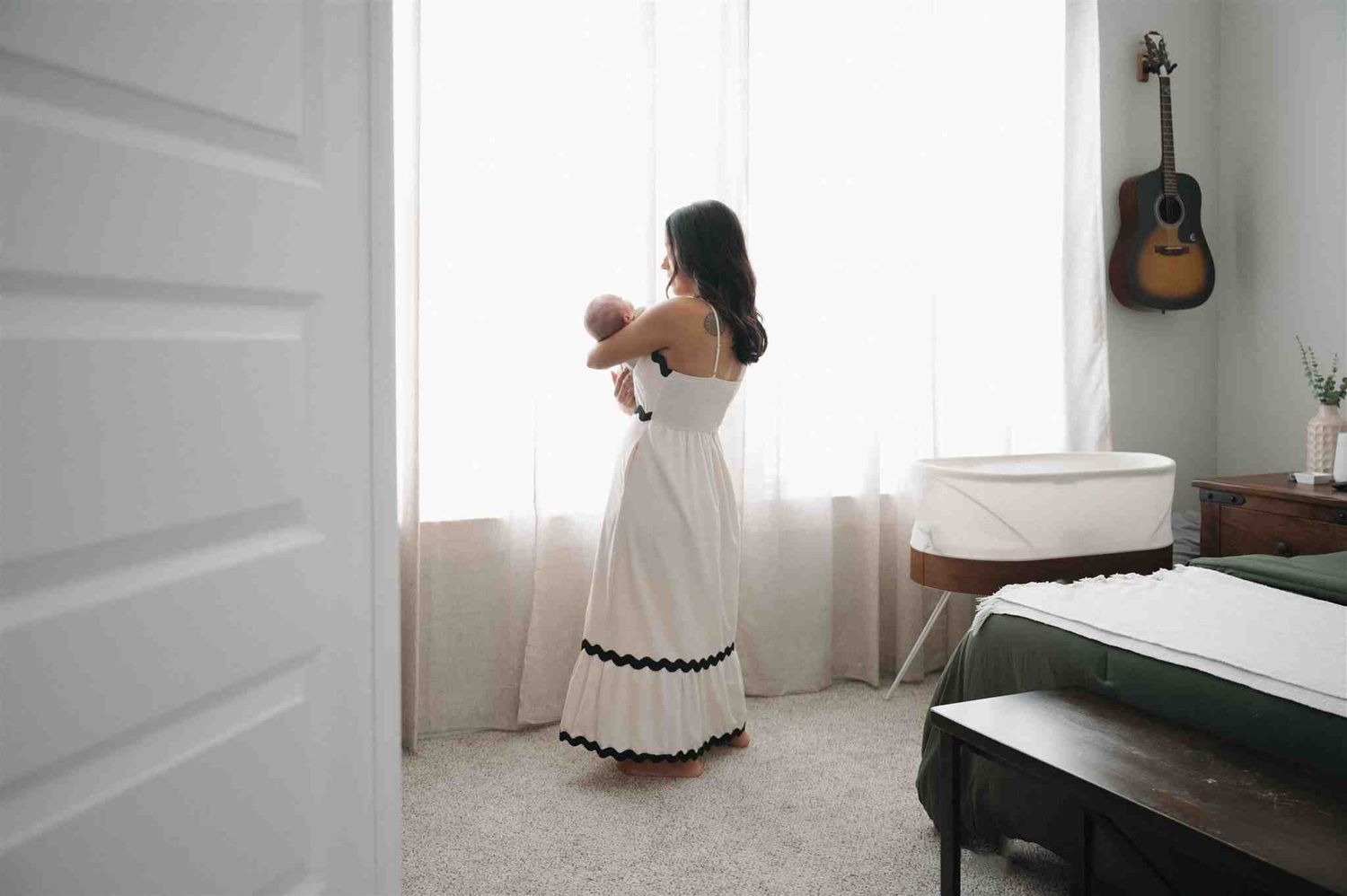 A white dress contrasts beautifully in a bright room with a bed and acoustic guitar hanging on the wall.