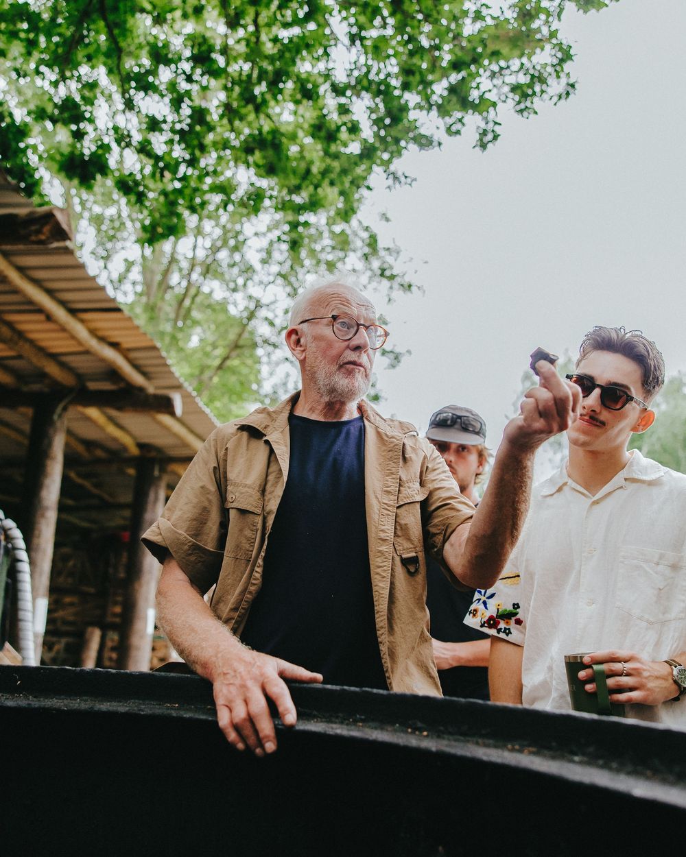 Two people in conversation outdoors with green trees visible in the background.