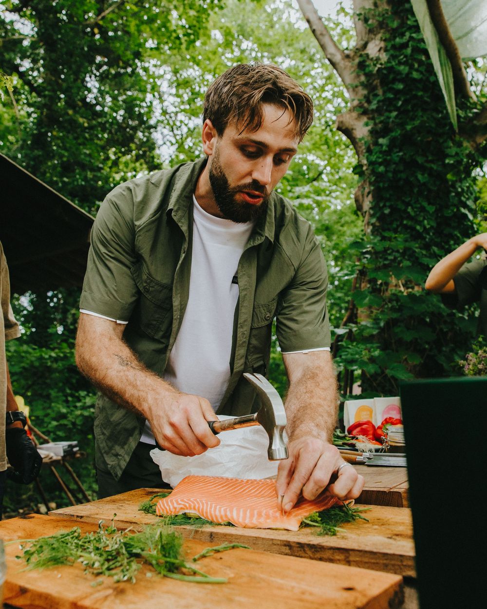 Someone carefully chops fresh herbs on a wooden cutting board in an outdoor kitchen setting.