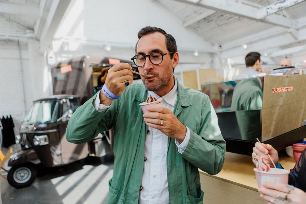 Person in mint green jacket tastes coffee during a tasting event.