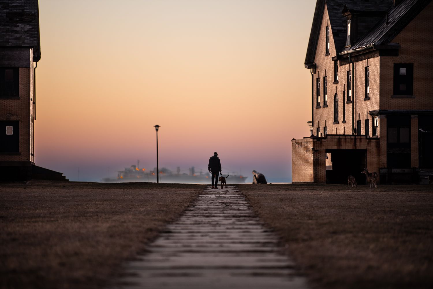 Silhouette of a person walking with a dog at sunset between buildings of Officers Row in Fort Hancock Sandy Hook NJ
