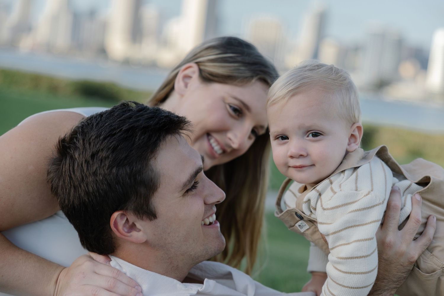 Family enjoying a tender moment outdoors with city skyline visible behind them.
