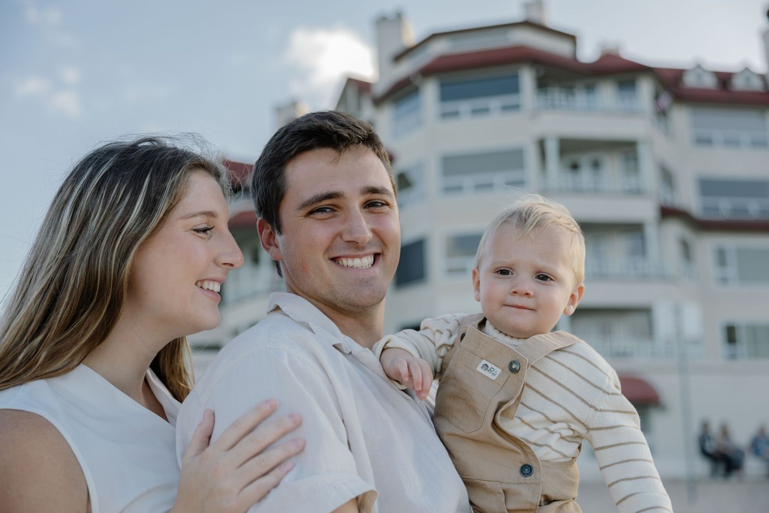 Young family poses together outdoors with apartment building in background.