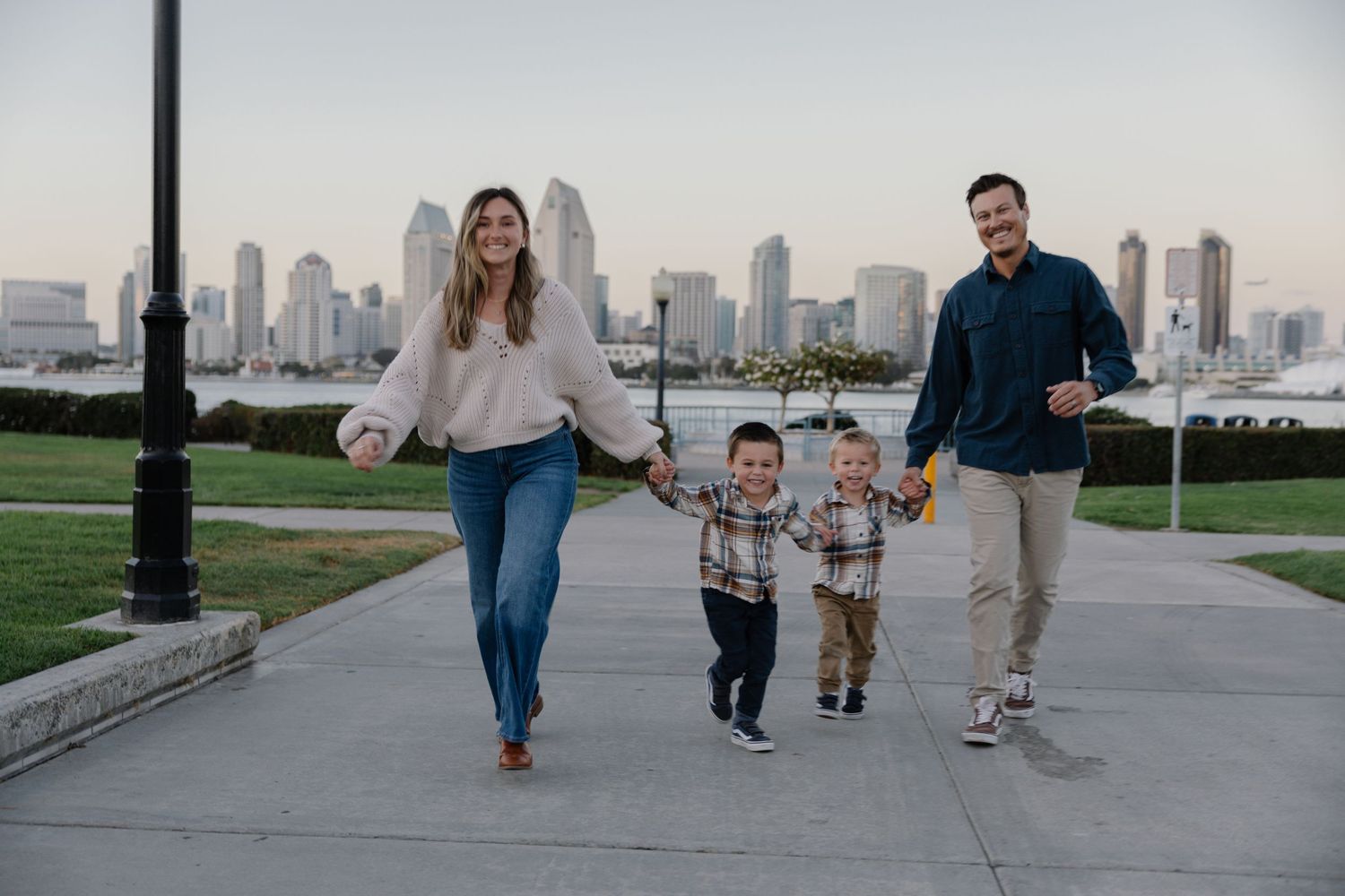 Family running together on waterfront path with urban skyline in background.