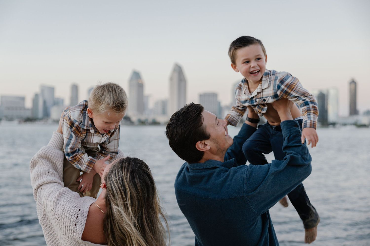 Family sharing playful moment together by waterfront with city views.