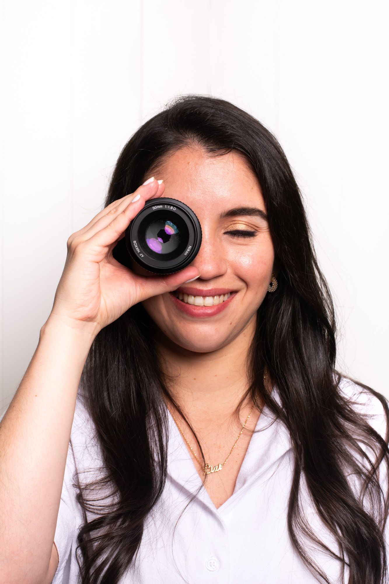 Creative portrait of photographer looking through camera lens against white background.
