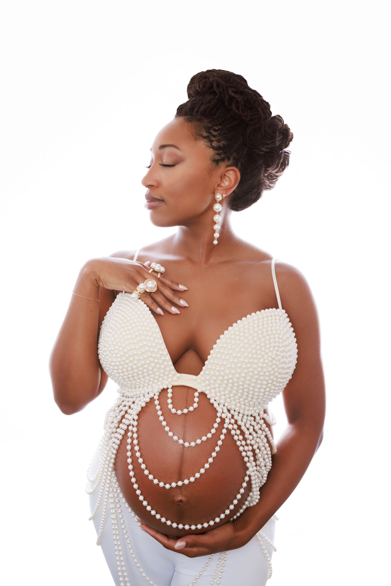 Elegant maternity photo featuring a white pearl-adorned top and stylish updo hairstyle against white background.