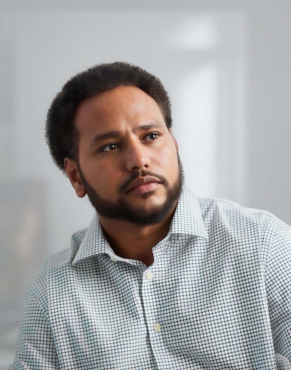 Professional headshot of person wearing a checkered button-up shirt against a light background.