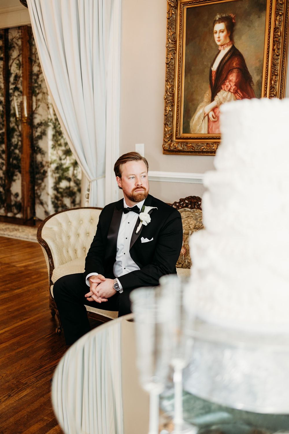 groom looking out the window in front of the wedding cake