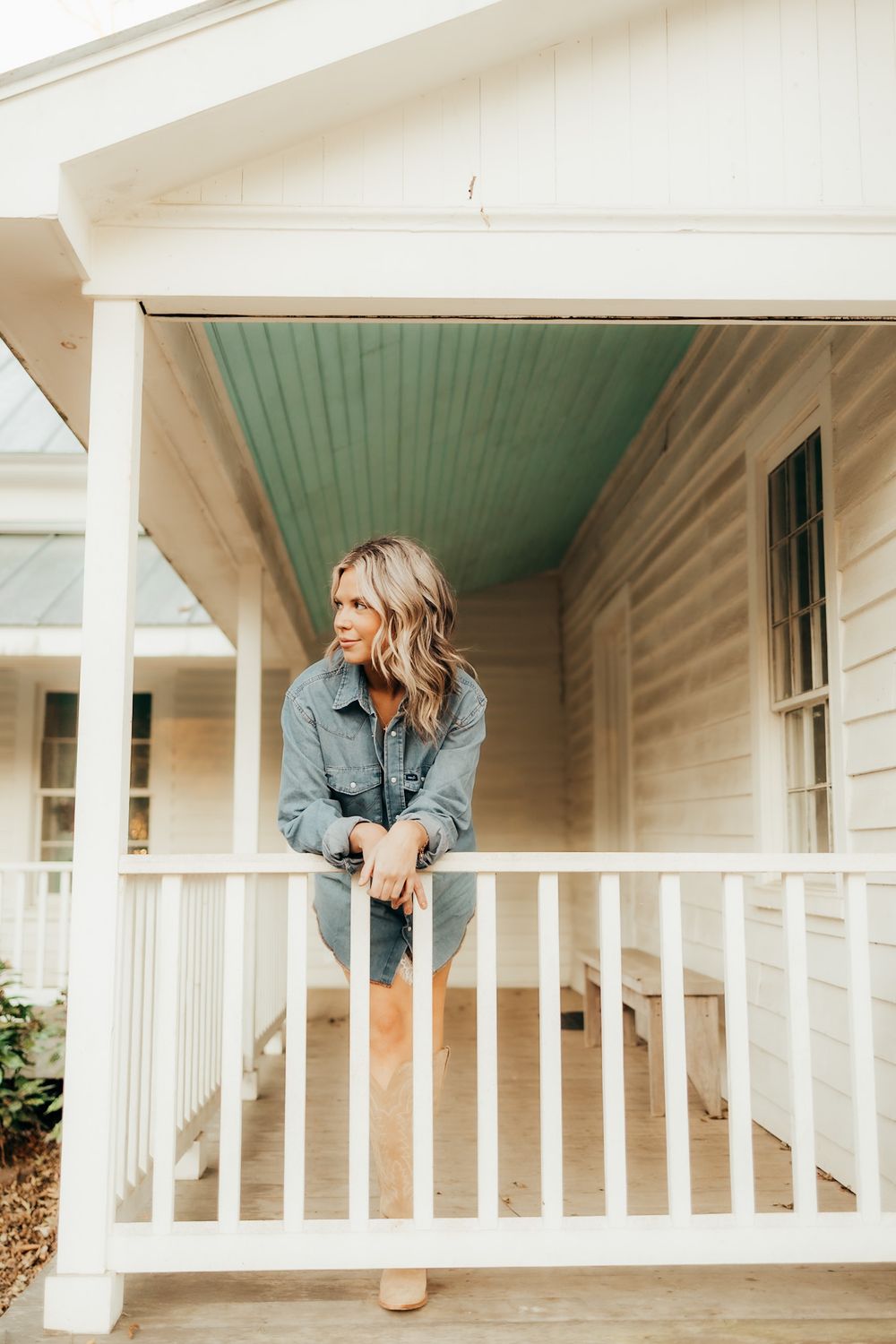 girl leaning over the railing of a white house looking off to the side