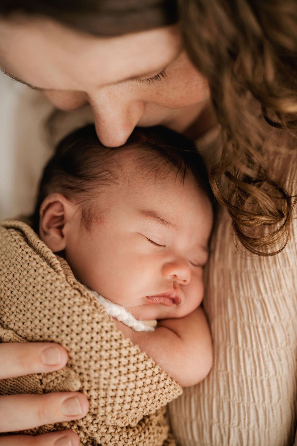 Peaceful sleeping newborn wrapped in knitted blanket during intimate portrait session.