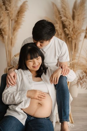A series of maternity photos showing a pregnant belly against a backdrop of dried pampas grass in a minimalist setting.
