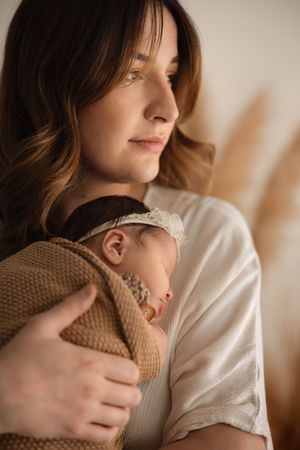 Tender moment captured in warm tones as parent cradles sleeping newborn against brown knit sweater.