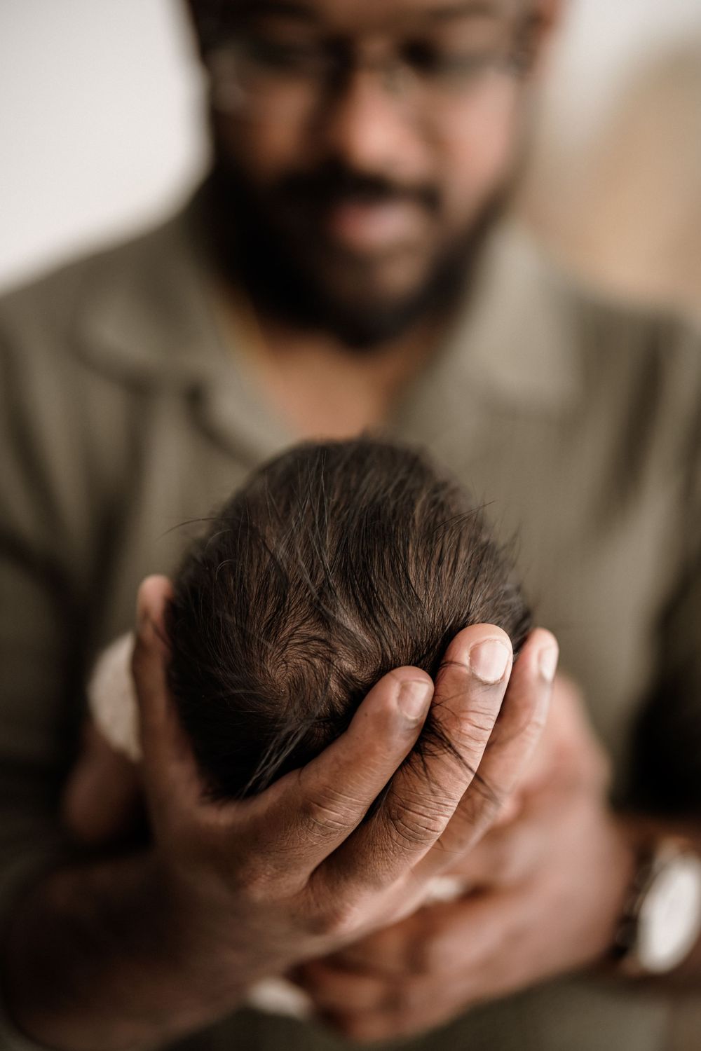 A tender moment captured as gentle hands cradle a newborn baby's head with soft focus and warm tones.