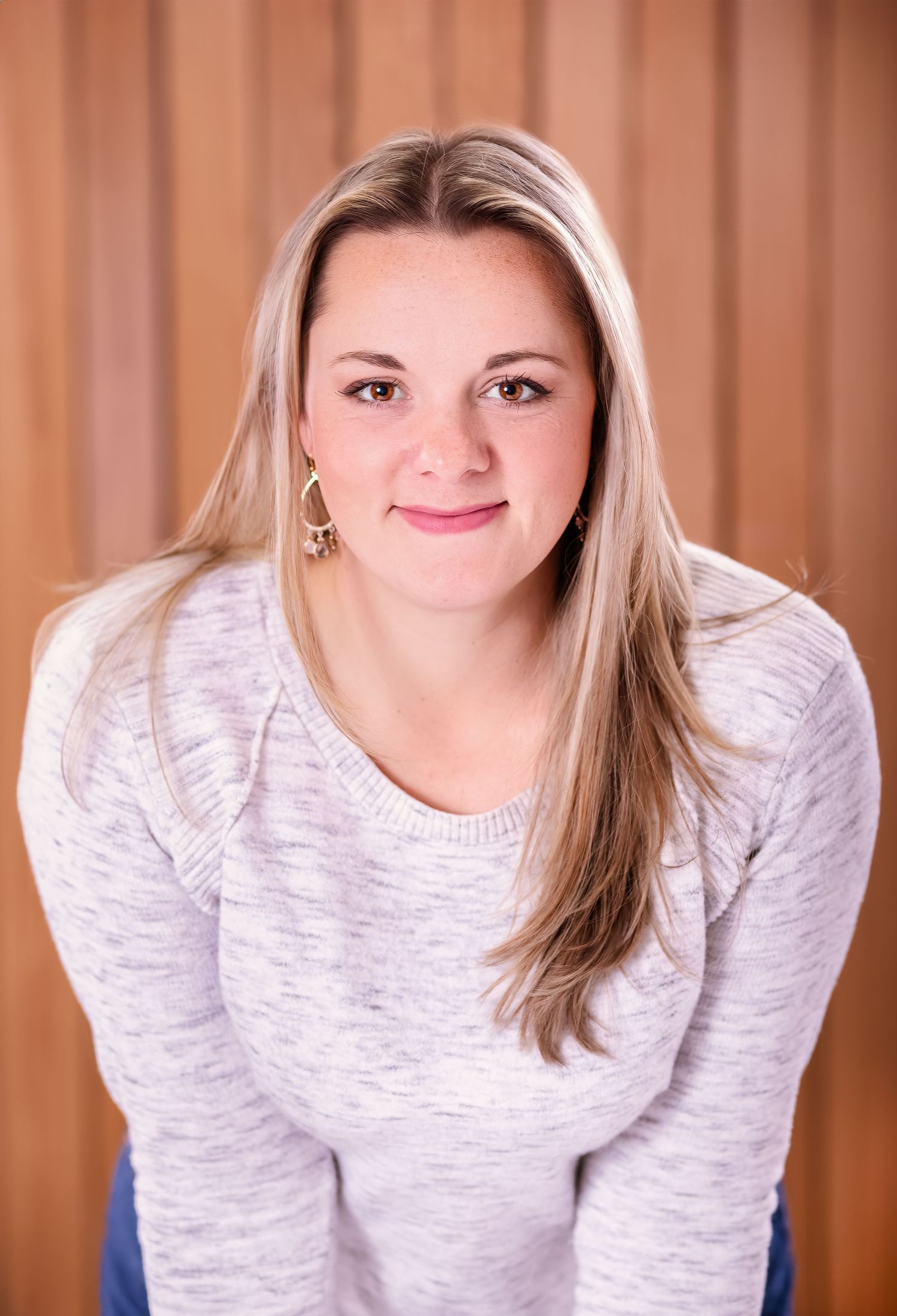 Portrait of a person in a white sweater against a wood panel background.
