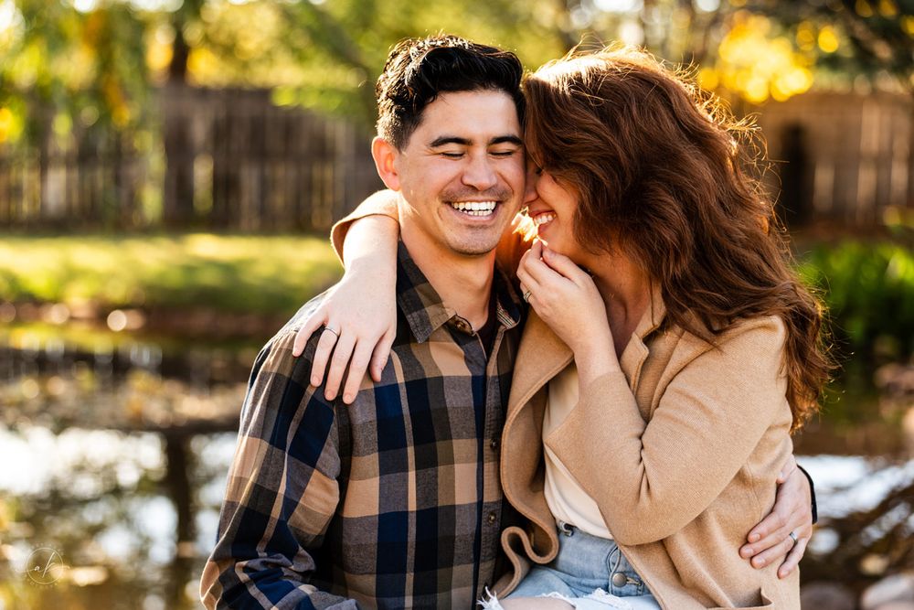 Romantic couple sharing a laugh together in golden sunset light against a garden backdrop.