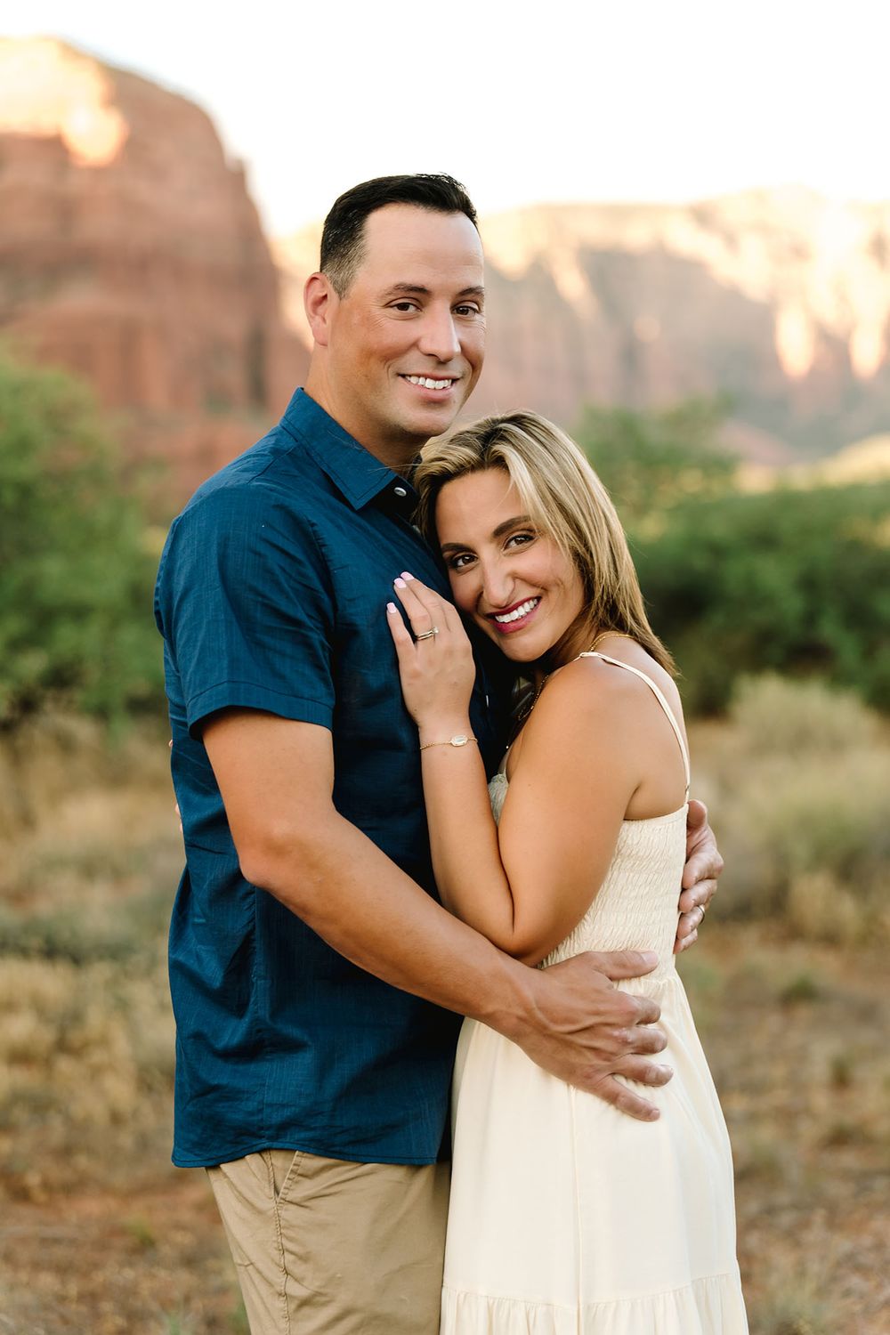 Smiling couple embracing outdoors with Sedona red rock formations glowing in golden hour light.