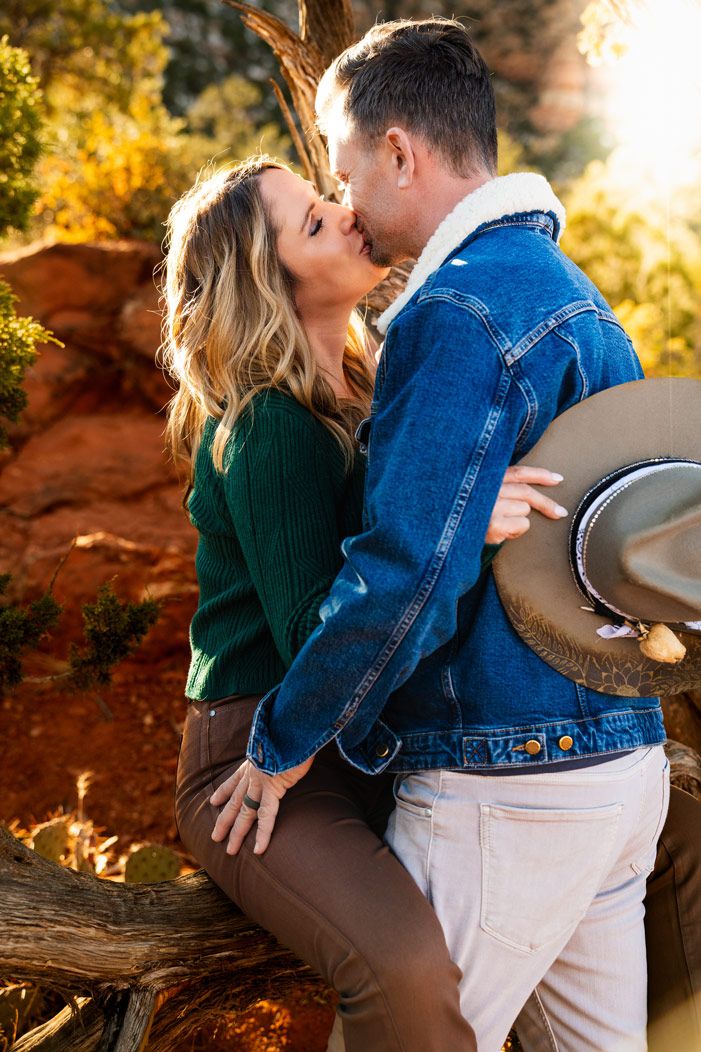 Couple sharing a romantic kiss against Sedona red rocks during golden hour.