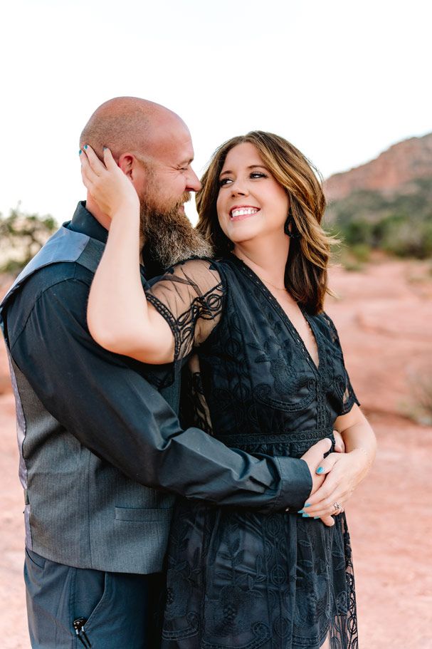 Couple in formal black attire embracing against Sedona desert landscape backdrop.