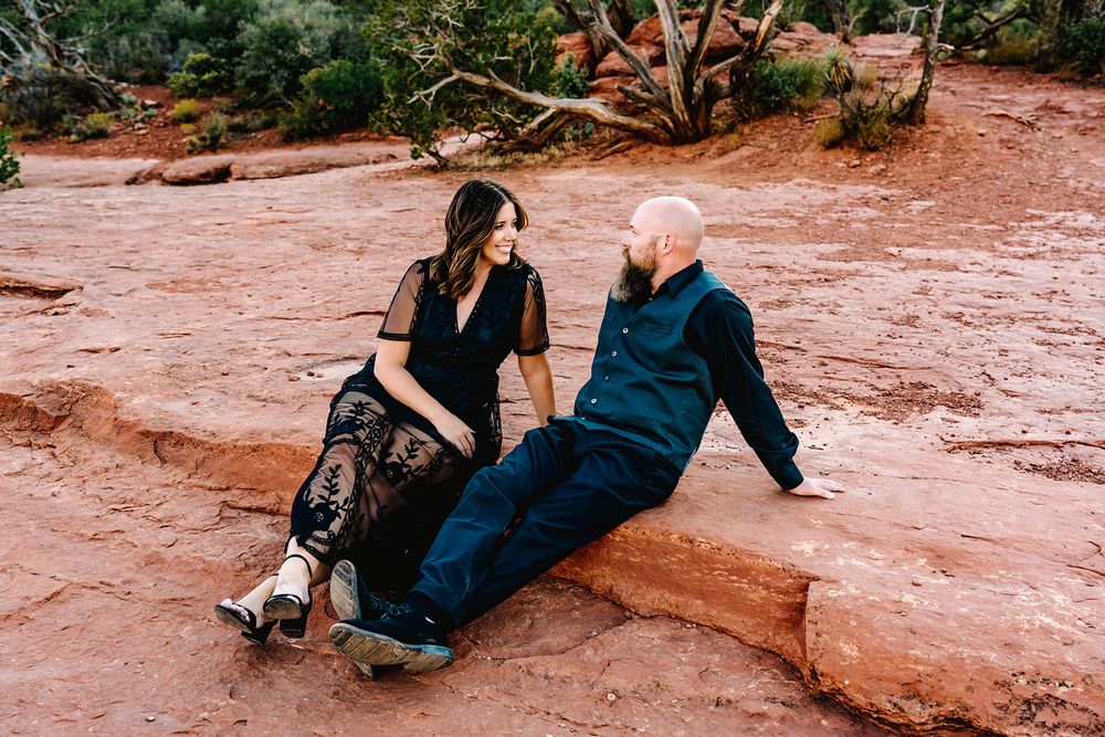 Couple sitting together on red rock formations in Sedona, Arizona, wearing dark outfits, sharing a romantic moment.