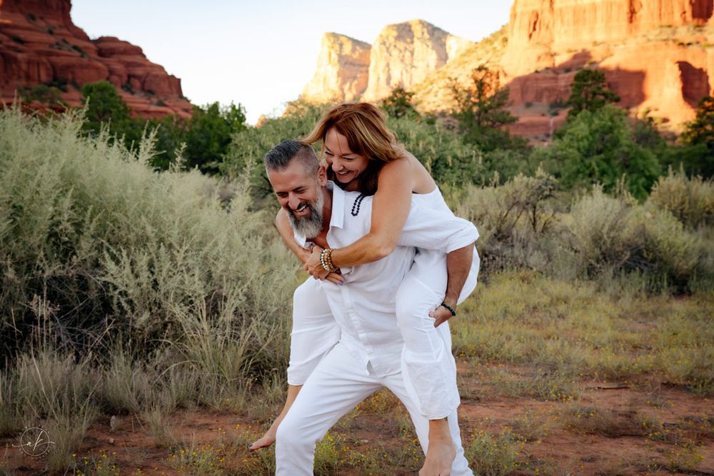 Playful couple in white clothing enjoying moment against Sedona red rock formations.