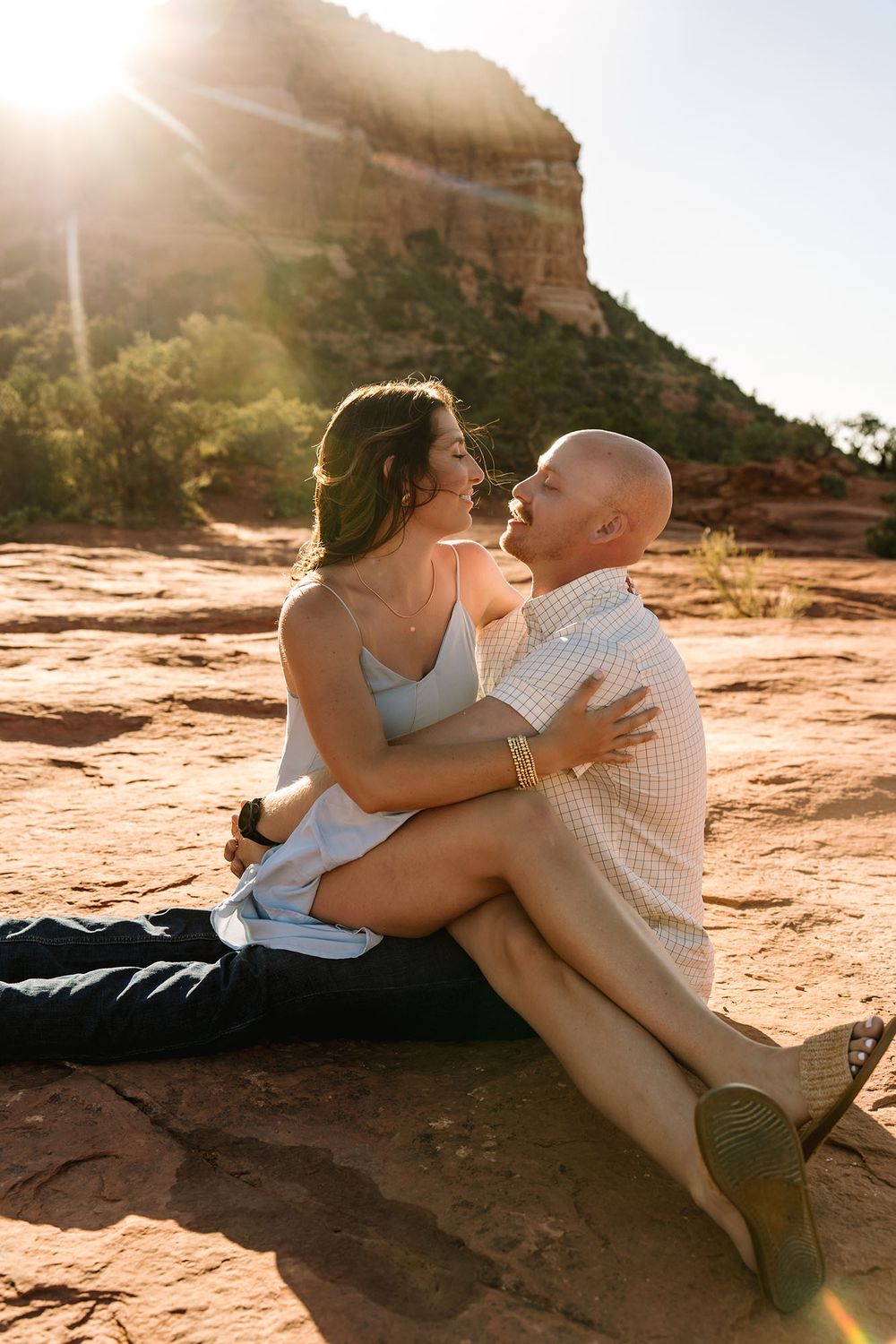 Couple sitting on red rocks in Sedona, Arizona, embracing and gazing at each other with golden sunlight behind them.