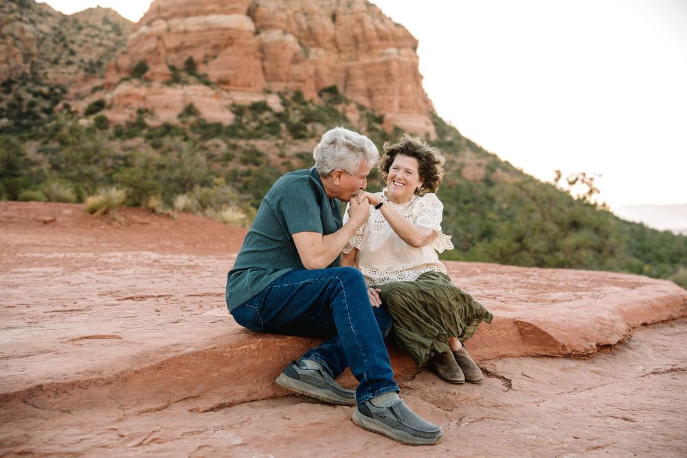 Older couple sitting on red rocks in Sedona, sharing a tender moment with red rock formations behind them.