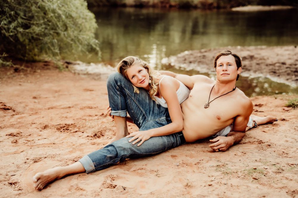 Casual couple lounging together on Sedona red sand near calm water.