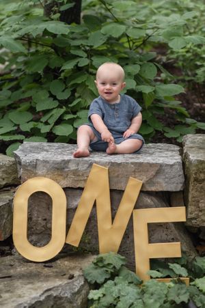 Large gold letters spelling ONE sit on stone steps with greenery in the background.