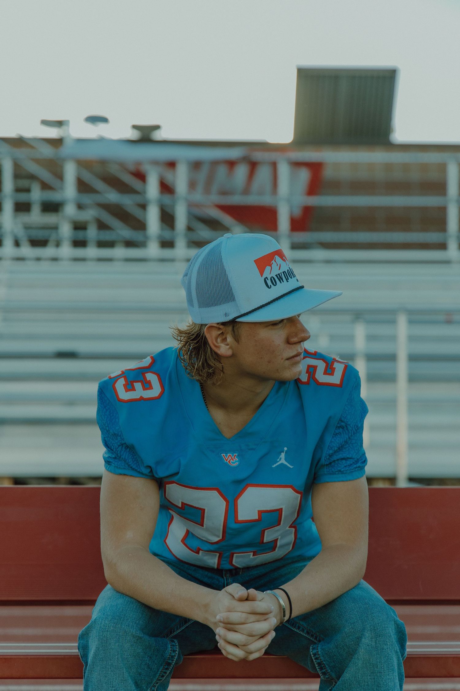 Highschool football player sitting on bench with hands folded together looking to the right