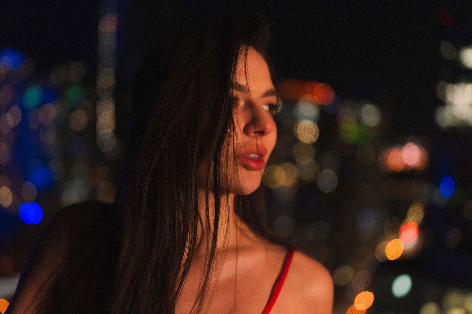 Nighttime portrait with blurred city lights creating a dreamy bokeh effect in the background.