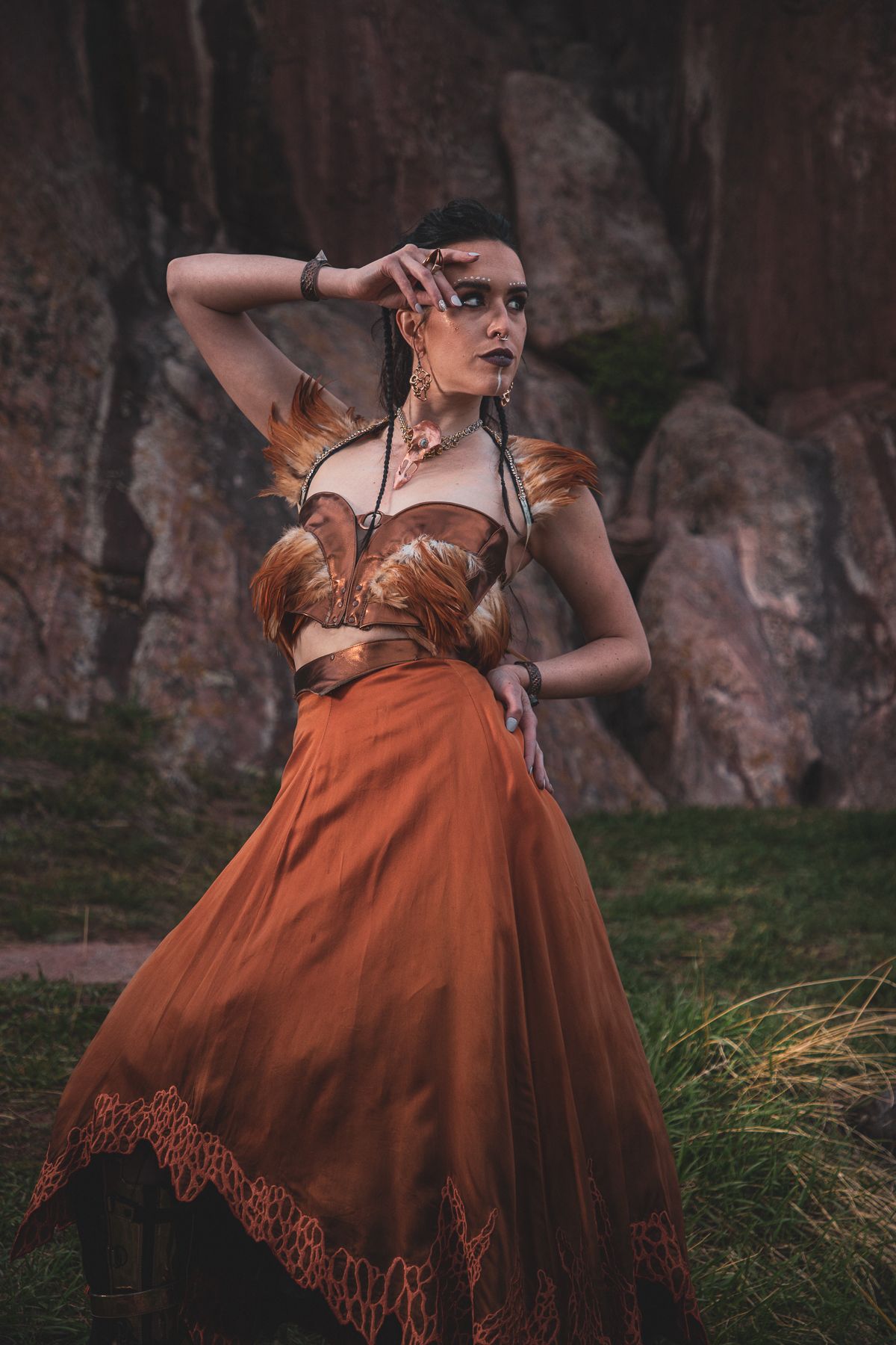 Artistic fashion portrait in brown corset dress against dramatic rock formation backdrop.