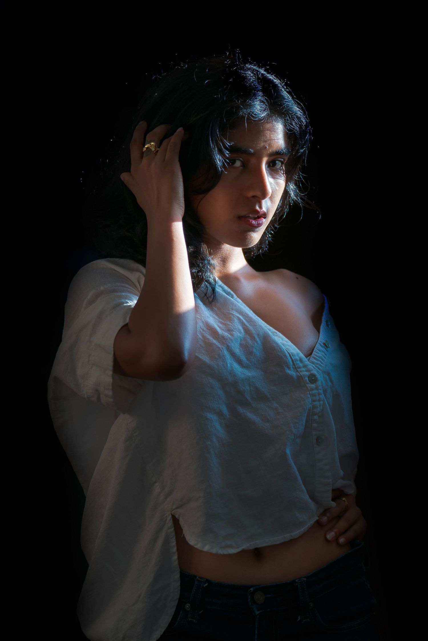 Dramatic portrait of person in white shirt against black background with moody lighting.