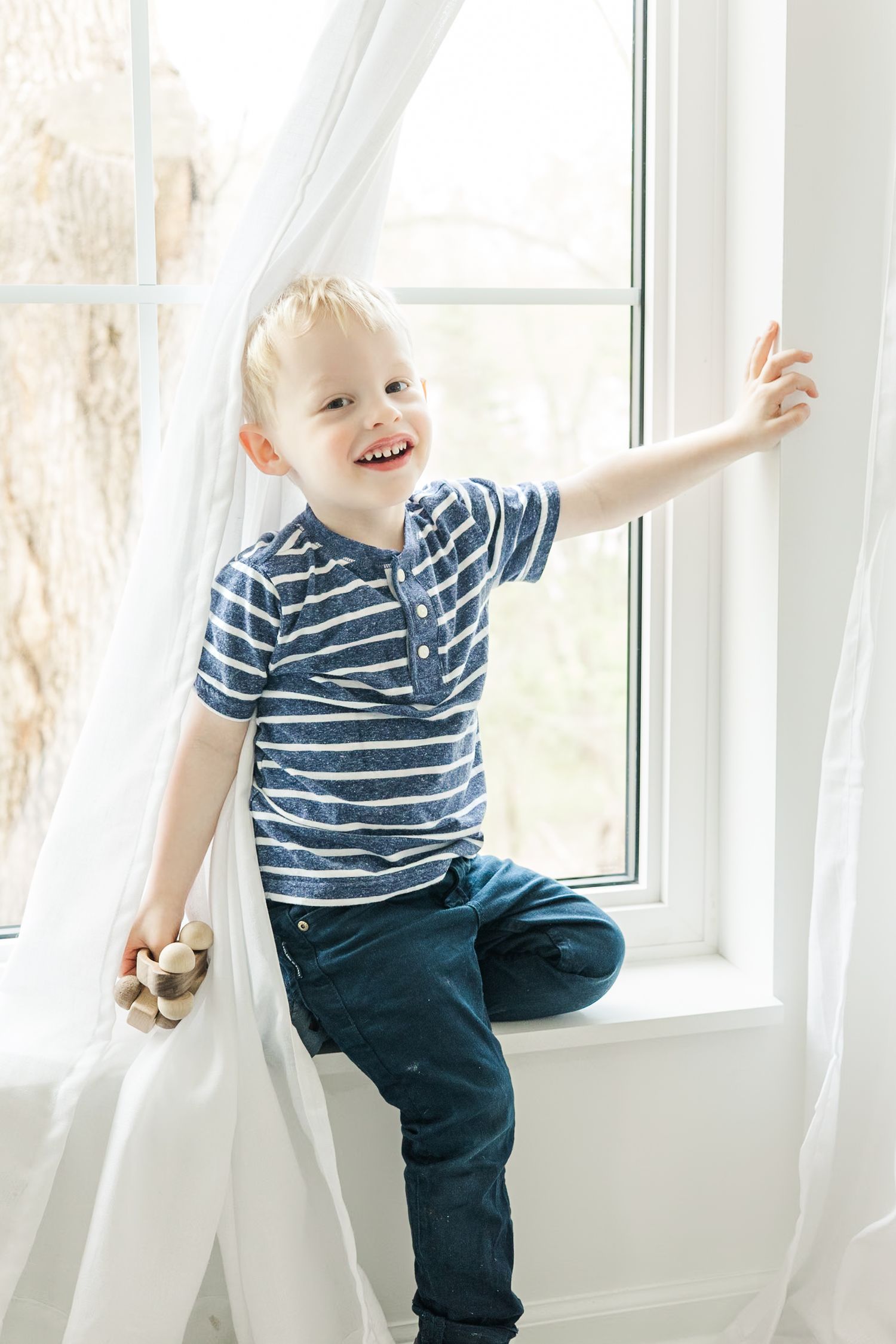 Playful sequence of a toddler in striped shirt laughing and playing by a bright window.