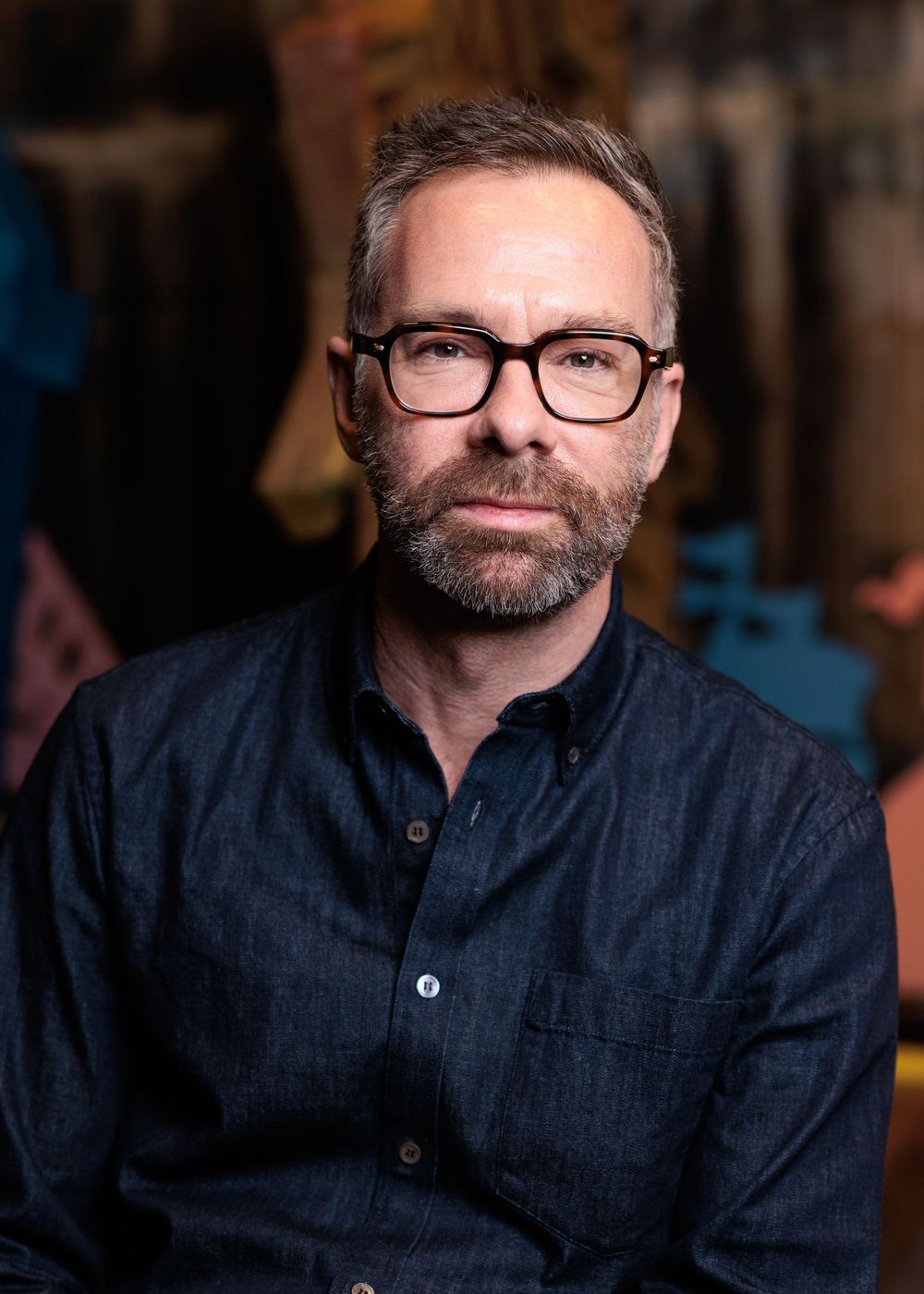 Professional headshot of person wearing glasses and navy shirt against blurred background.