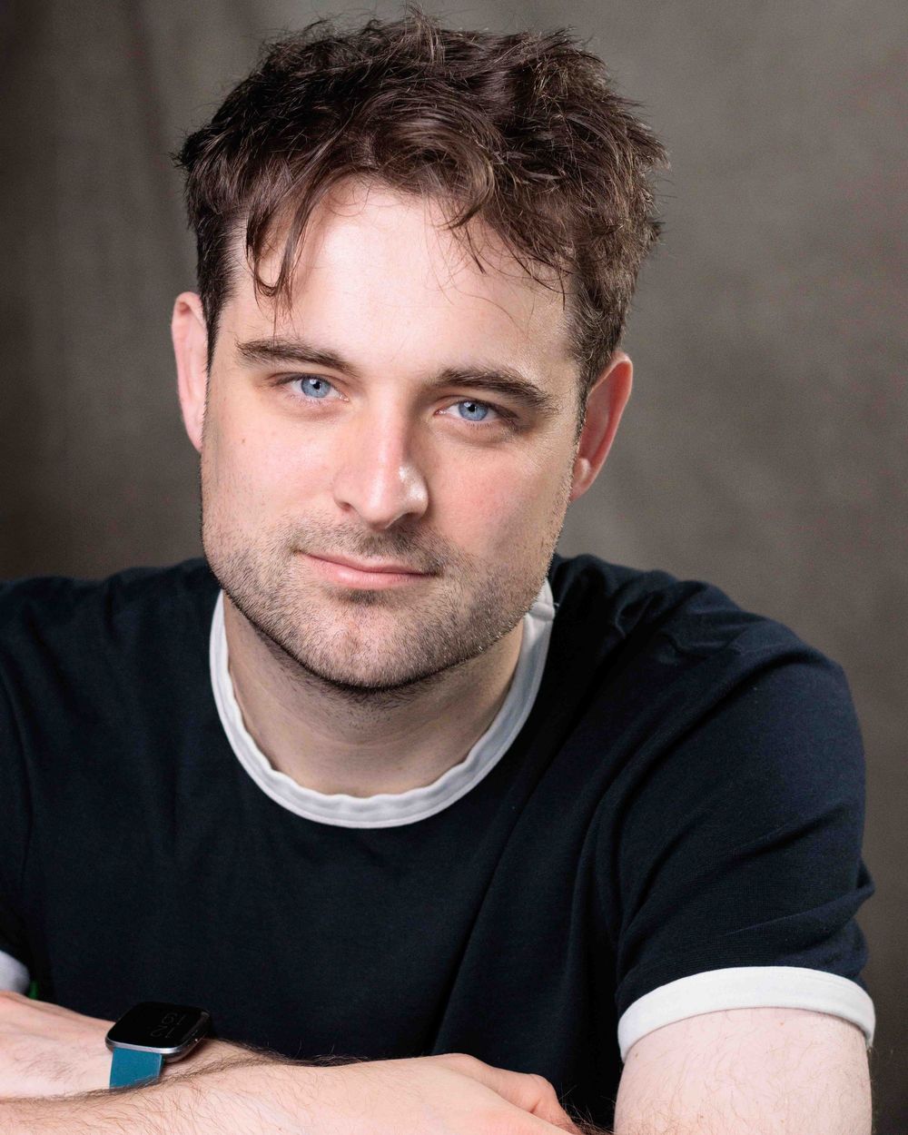 Professional headshot of a person wearing a navy sweater with white trim against a gray backdrop.