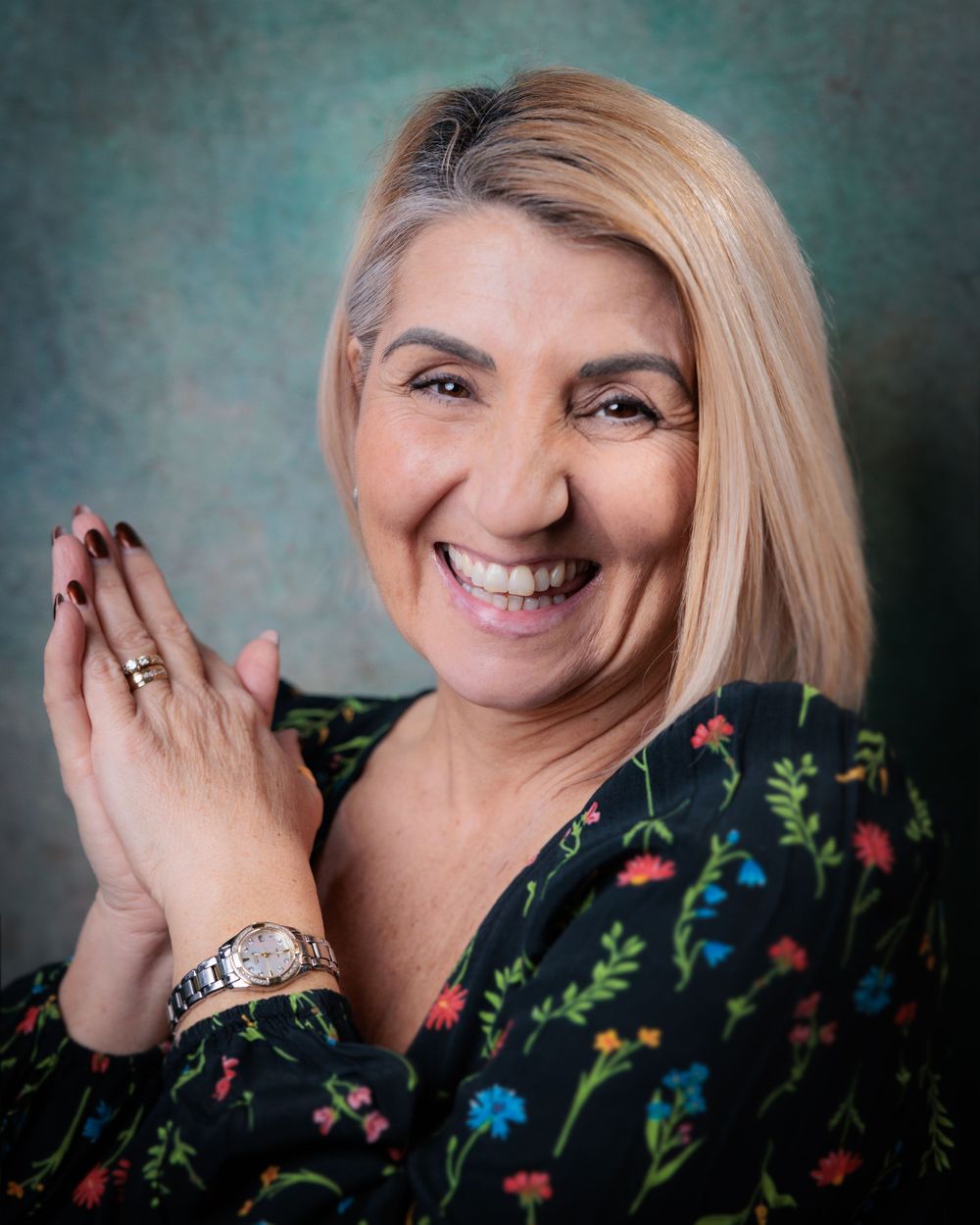 A person in a floral dress poses against a teal background in a series of expressive portraits showing joy and laughter.