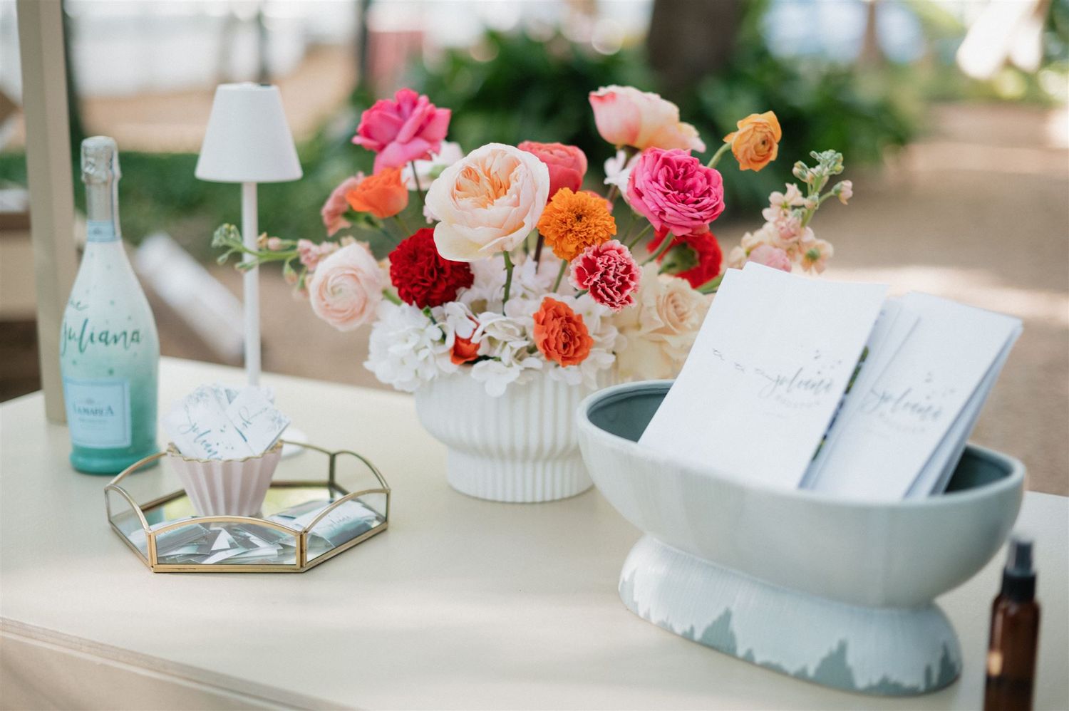 A romantic table setting with pink and coral roses in a white vase, a blue glass bottle, and decorative accessories.