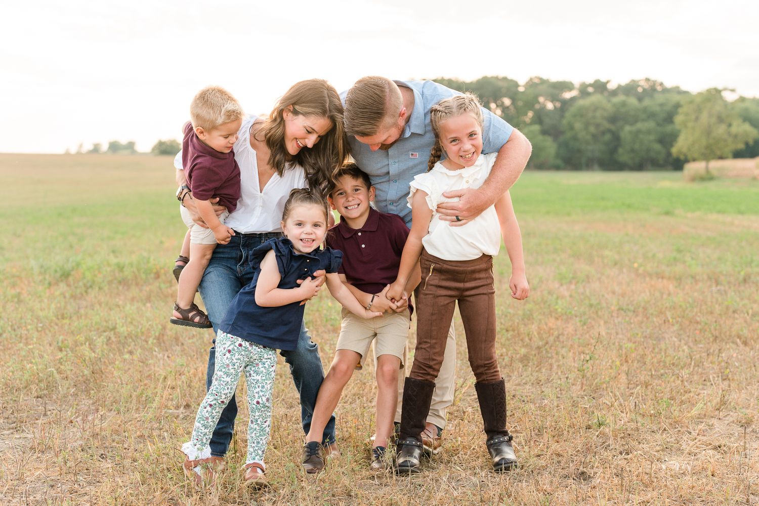 Playful outdoor family photoshoot in a rustic field setting.