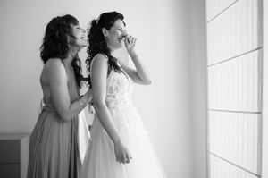 A joyful wedding moment captured in black and white as two figures share laughter by a bright window.